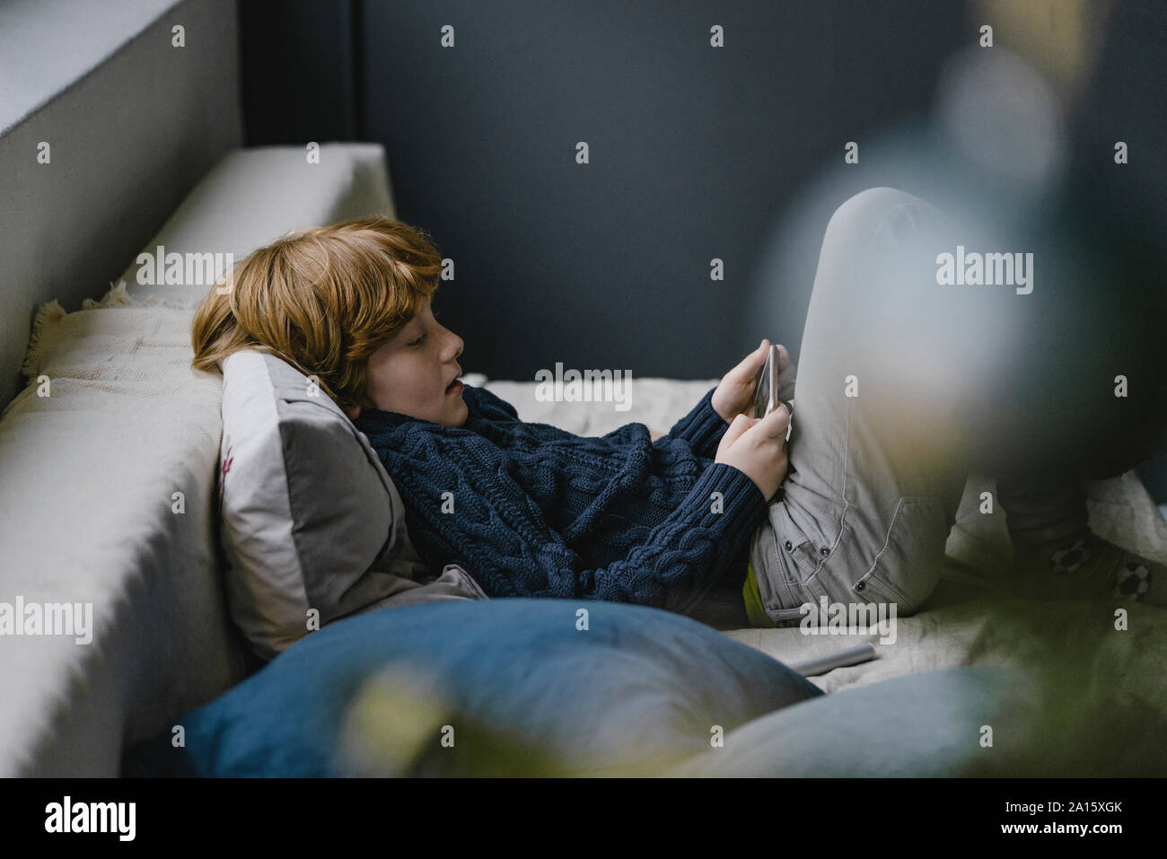 Redheaded boy lying on couch looking at cell phone Stock Photo