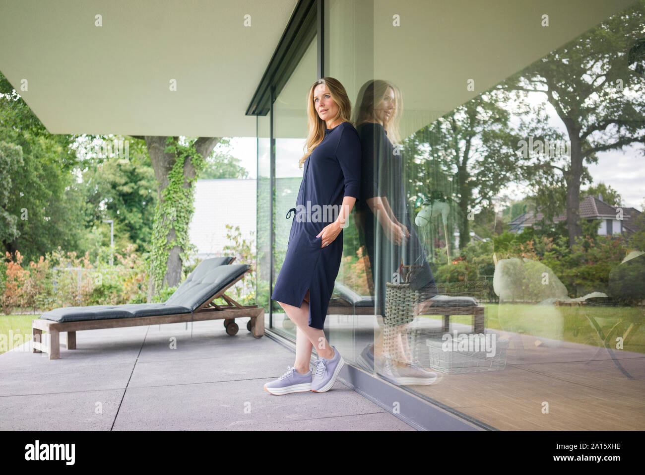 Woman leaning against the terrace door at home Stock Photo