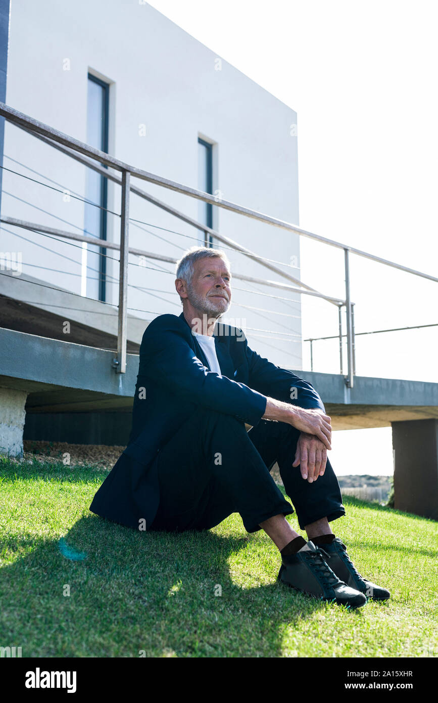 Senior businessman sitting on lawn outside a building Stock Photo