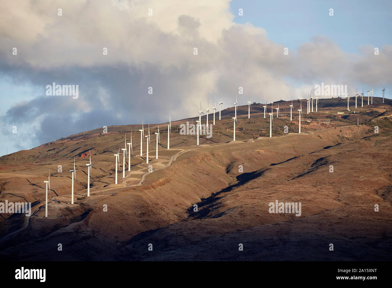 Wind turbines on hill against cloudy sky during sunset Stock Photo