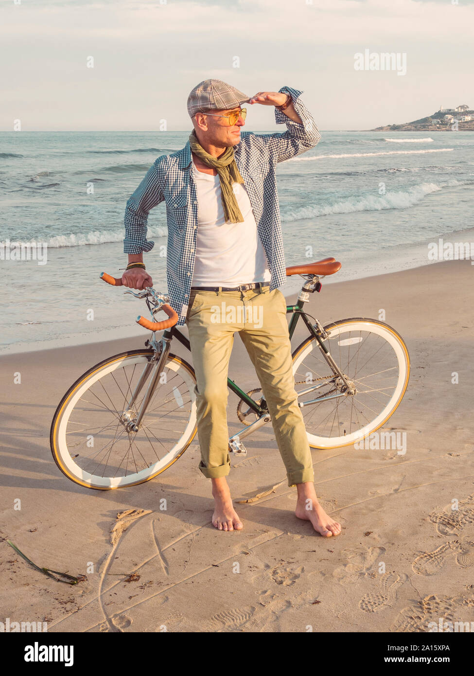 Barefoot man standing with Fixie bike on the beach looking at distance Stock Photo