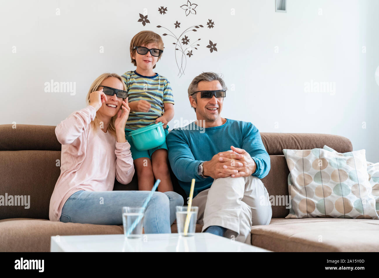 Father, mother and son wearing 3d glasses on couch at home watching Tv Stock Photo