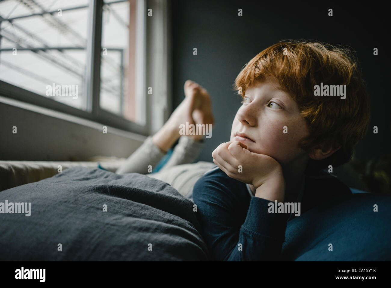 Portrait of redheaded boy lying on couch out of window Stock Photo