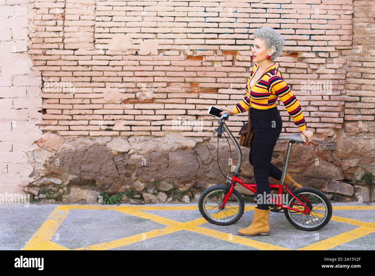 Fashionable mature woman with bicycle and smartphone on the street Stock Photo