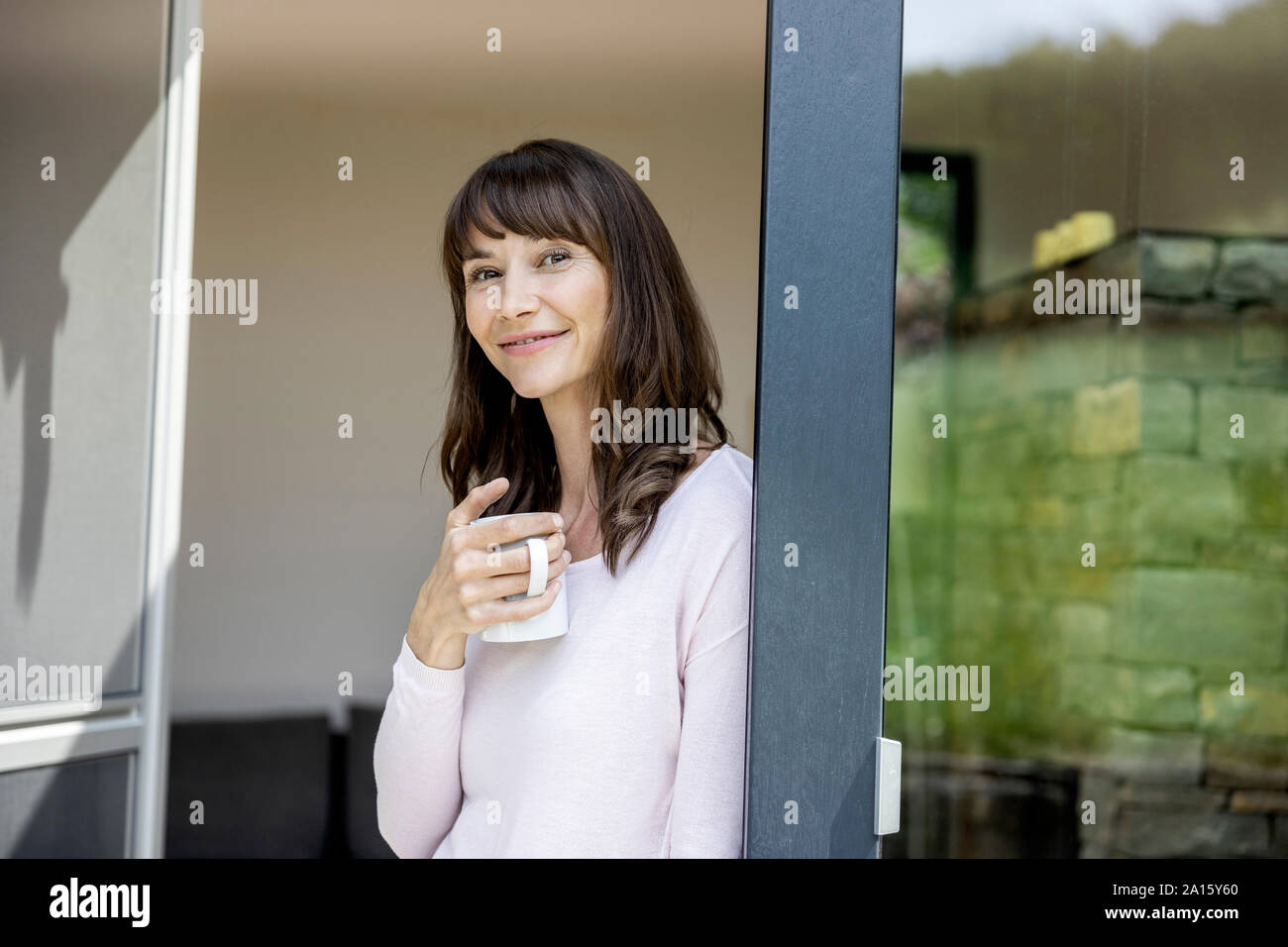 Portrait of smiling woman holding cup of coffee at home Stock Photo