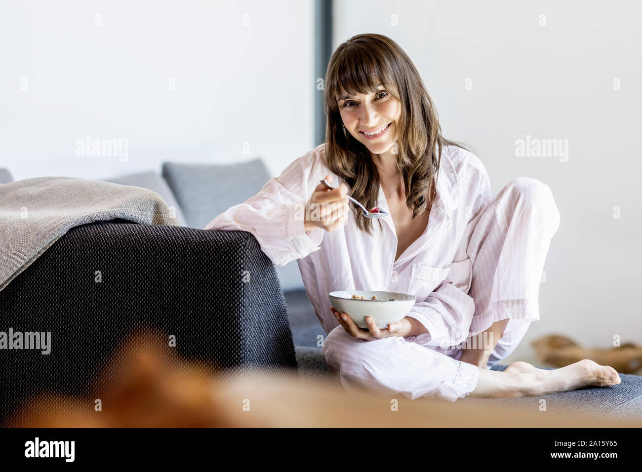 Portrait of smiling woman having breakfast on couch at home Stock Photo