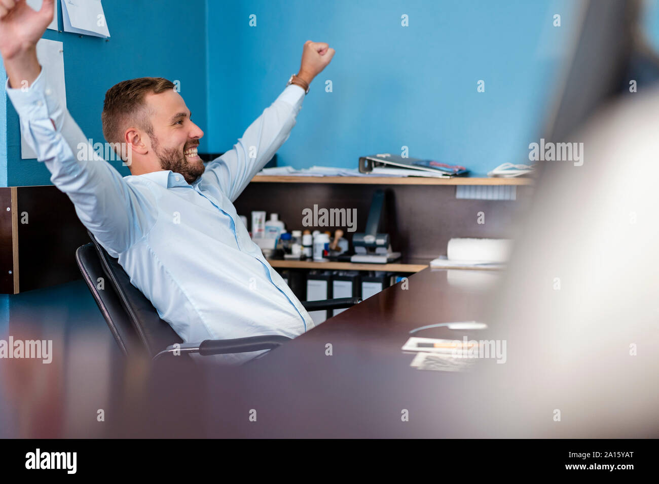 Happy businessman cheering at desk in office Stock Photo