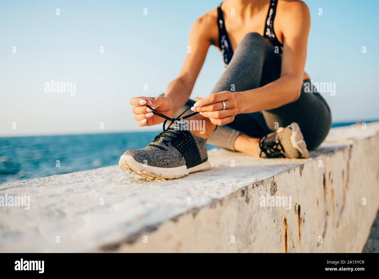 Sportswoman sitting on a wall and tying running shoe Stock Photo