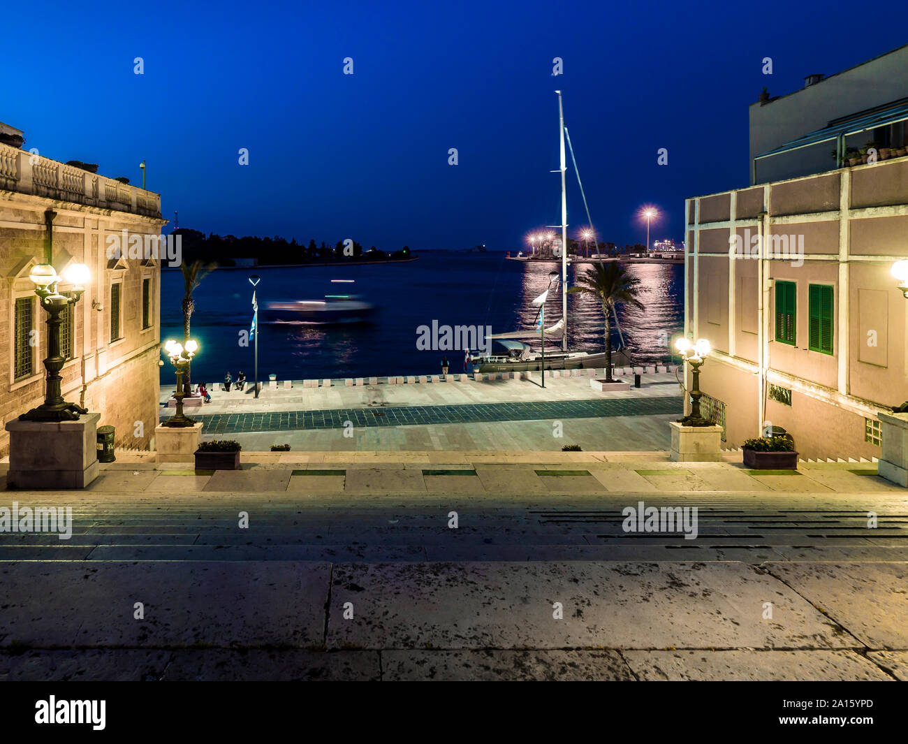 View of sea from steps amidst buildings against blue sky at night Stock Photo