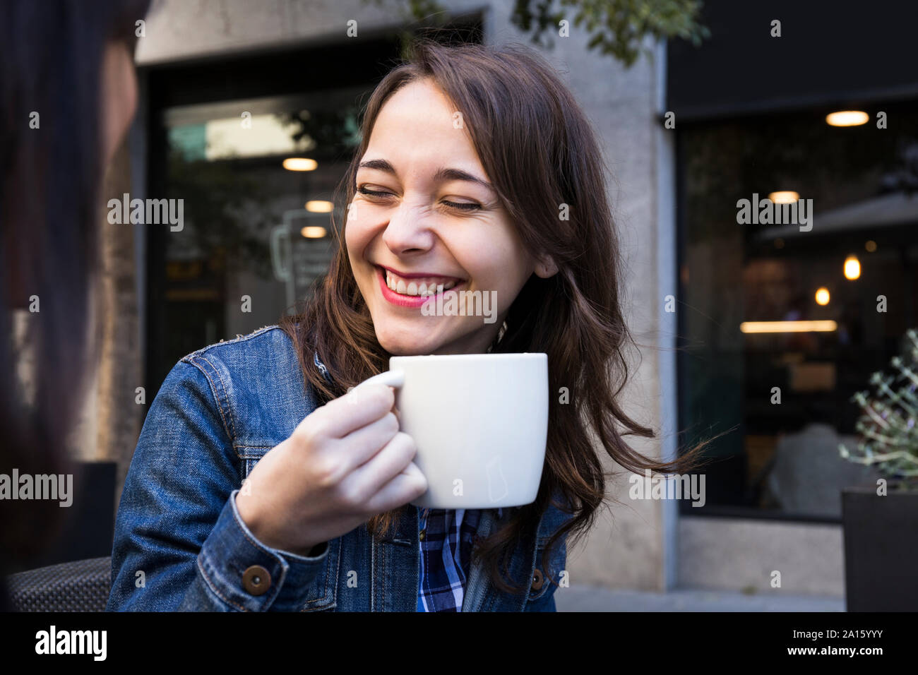 Happy young woman laughing with eyes closed and holding coffee cup in outside cafe in Madrid, Spain Stock Photo