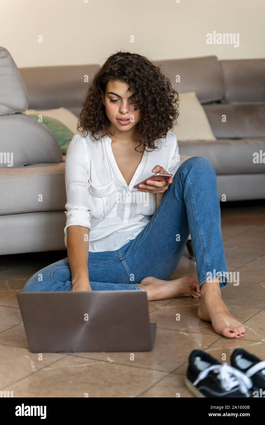 Young woman using cell phone and laptop at home Stock Photo