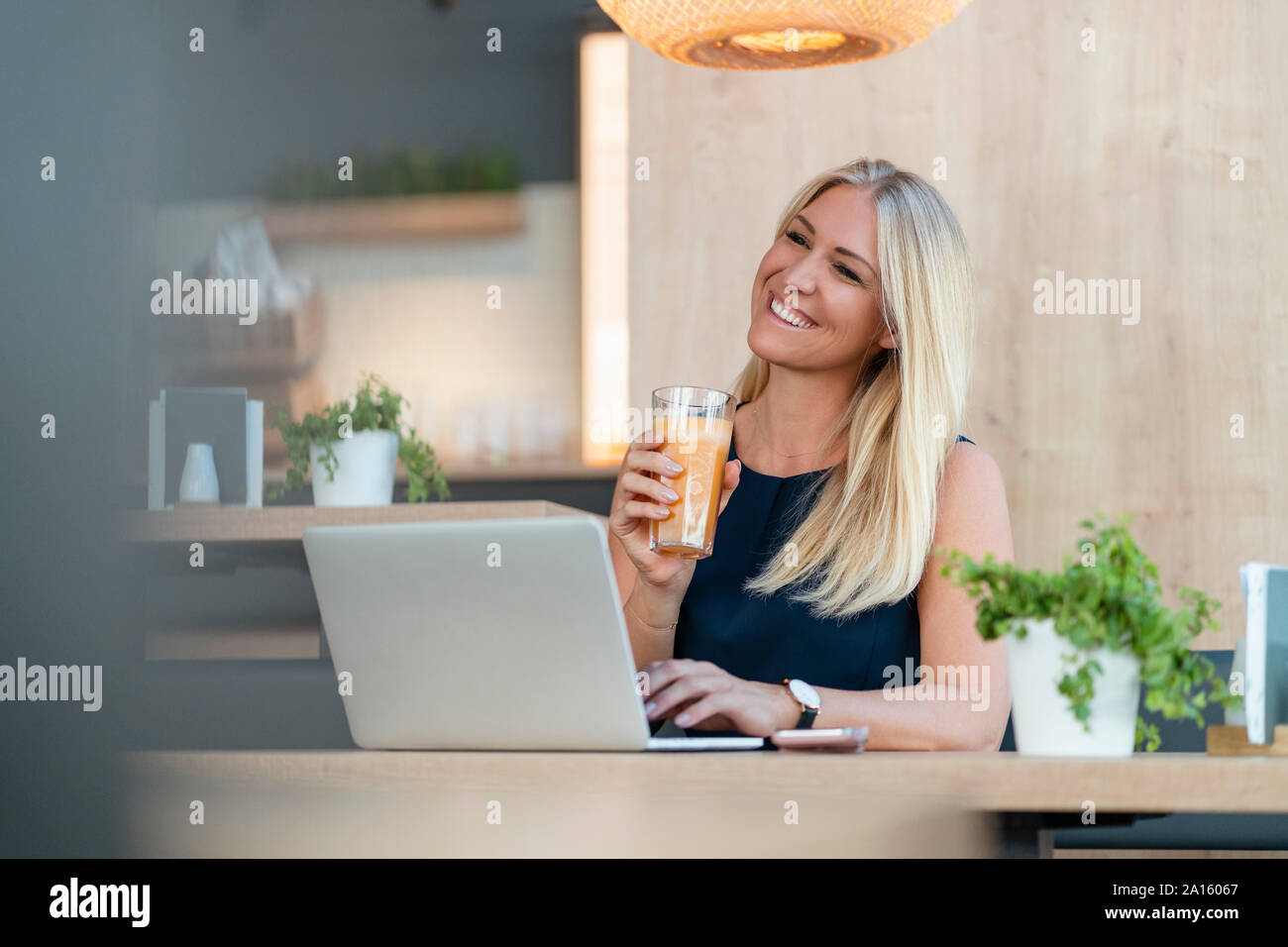 Portrait of smiling blond businesswoman with laptop and glass of orange juice in a coffee shop Stock Photo