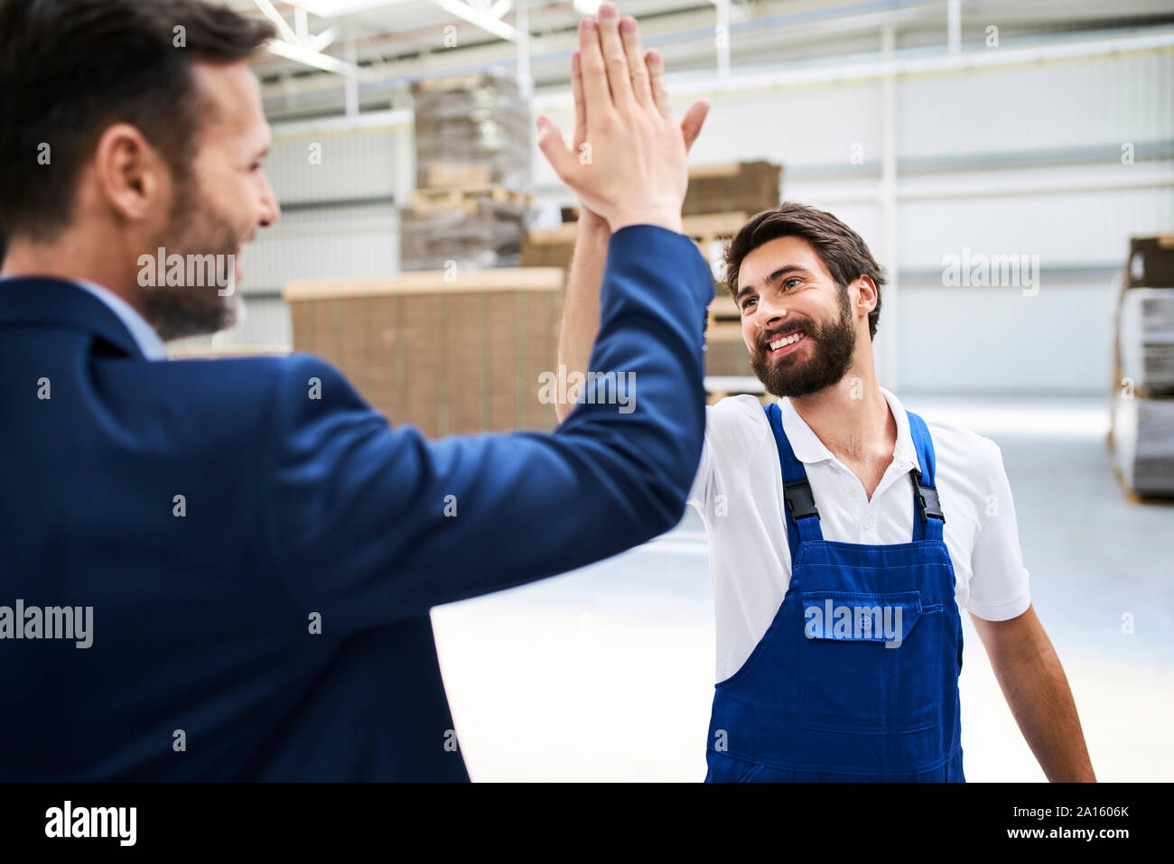 Happy businessman and worker high fiving in a factory Stock Photo