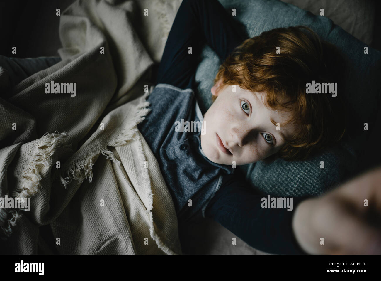 Portrait of redheaded boy lying on couch looking up Stock Photo