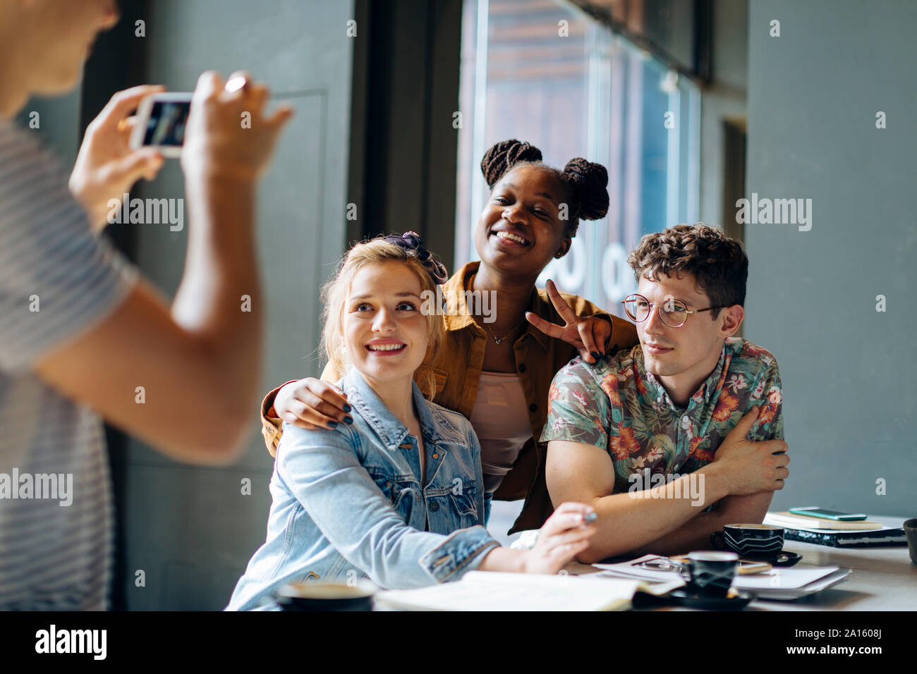 Students sitting in cafe, taking samrtphone selfies Stock Photo