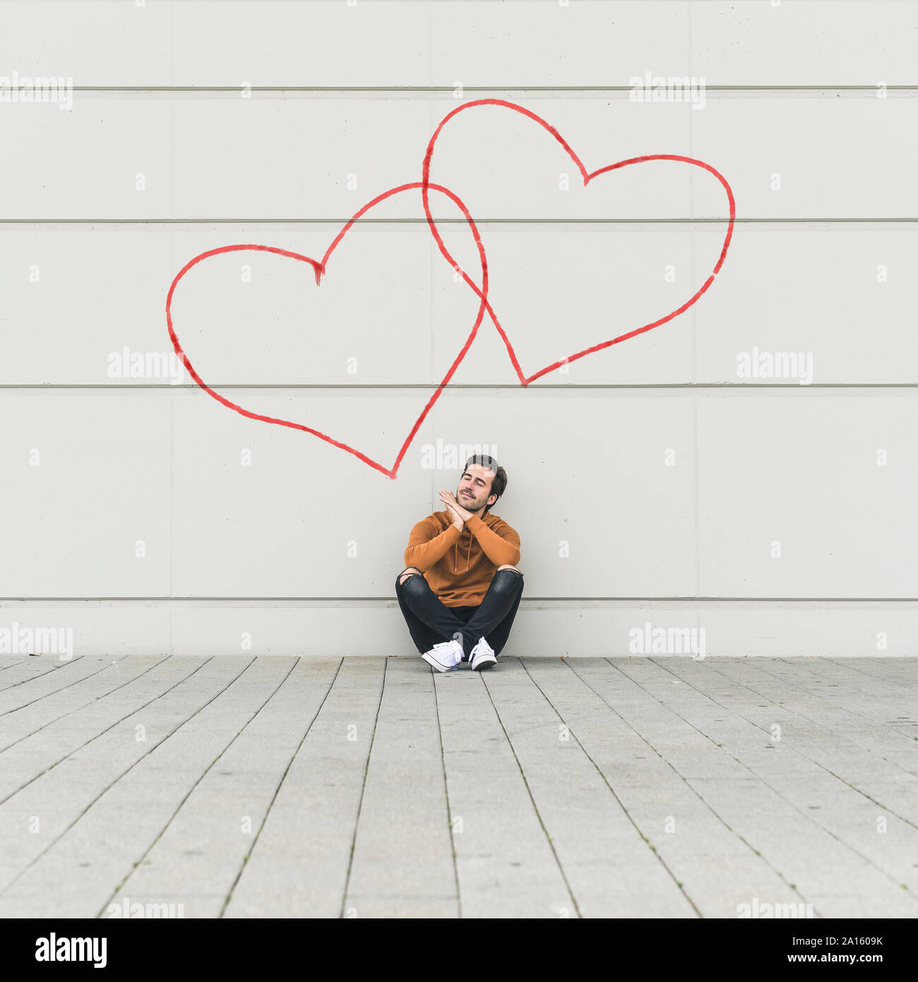 Digital composite of young man sitting at a wall with hearts Stock Photo