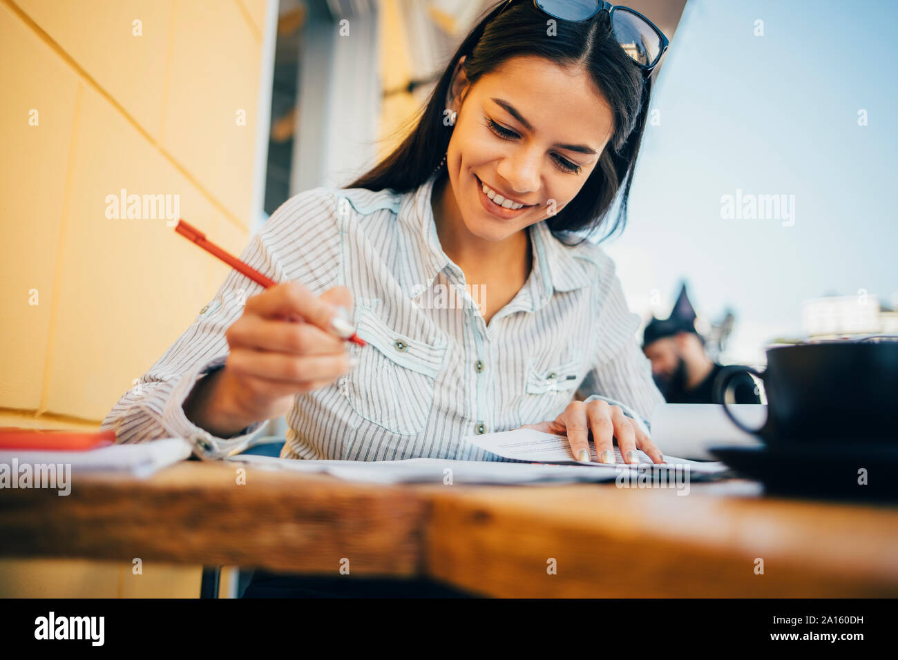 Smiling young woman taking notes in a cafe Stock Photo