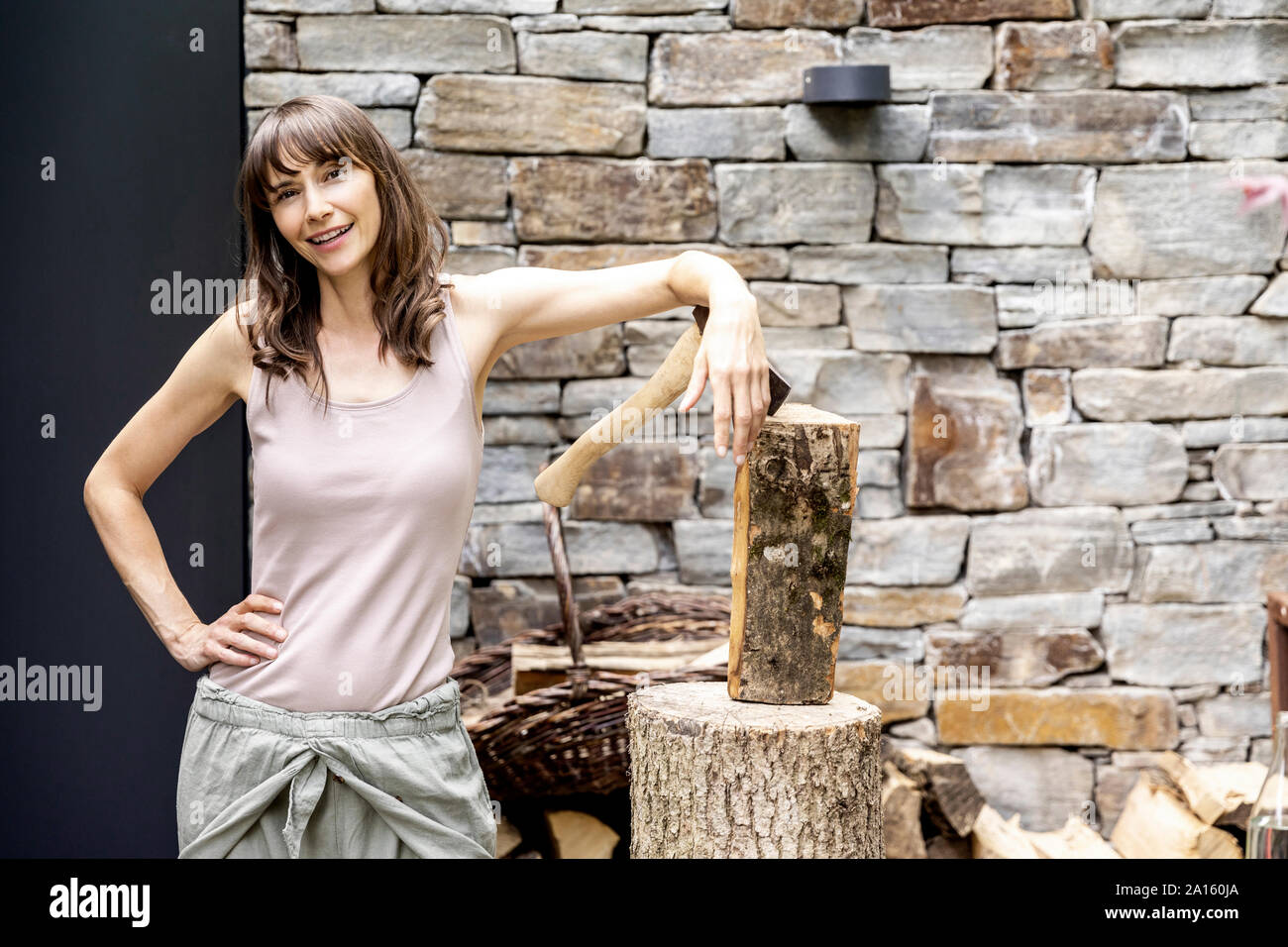 Portrait of confident woman with axe and firewood in front of a house Stock Photo
