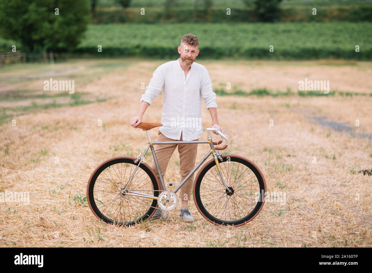 Man with handcrafted racing cycle on stubble field Stock Photo