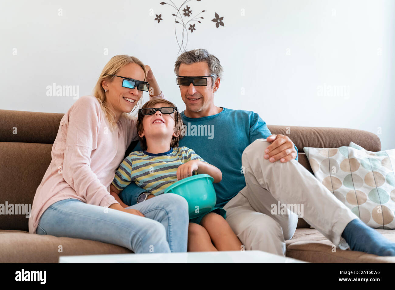 Father, mother and son wearing 3d glasses on couch at home watching Tv Stock Photo