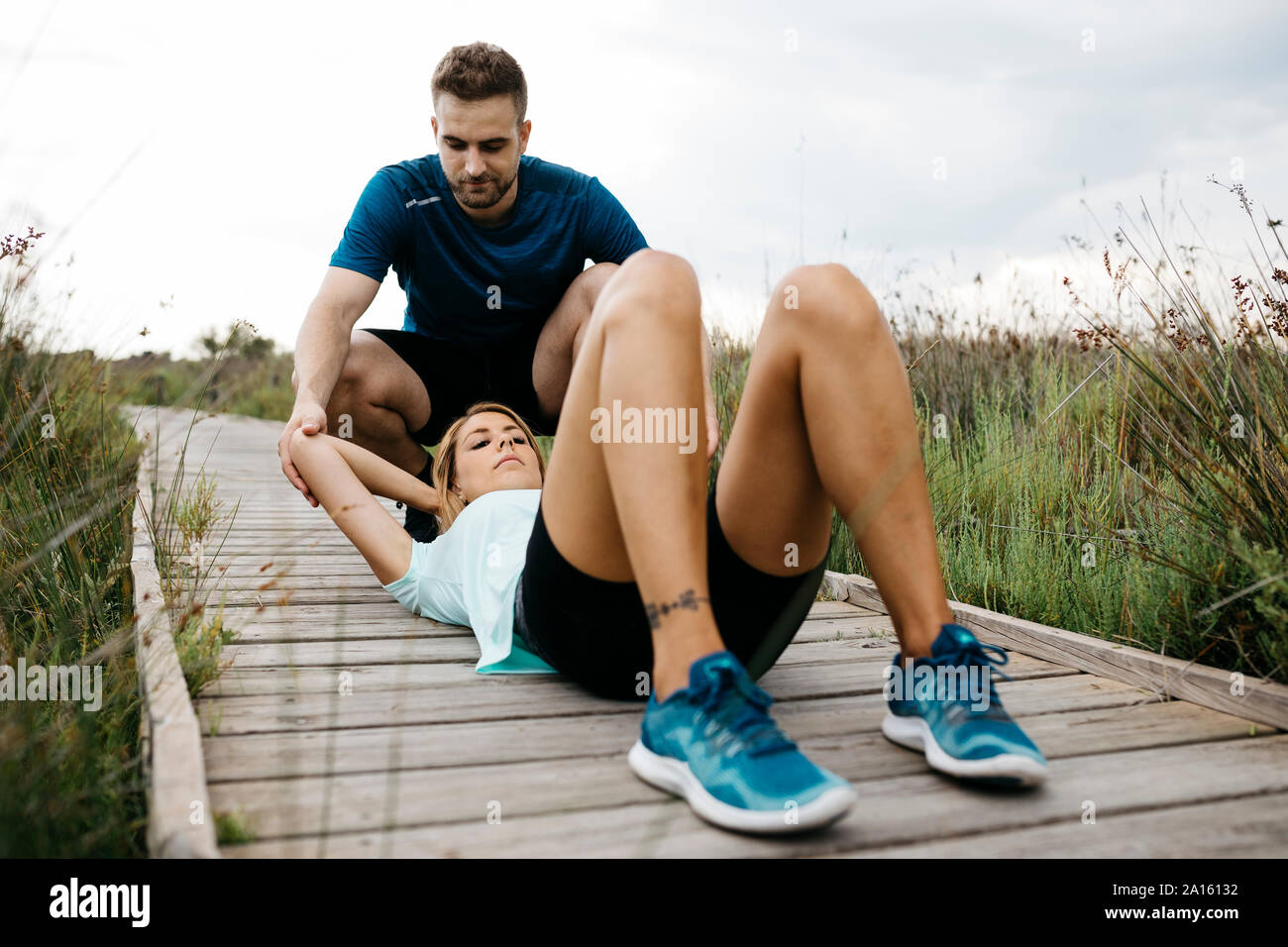 Female jogger training with her coach on a wooden walkway, sit-up Stock Photo