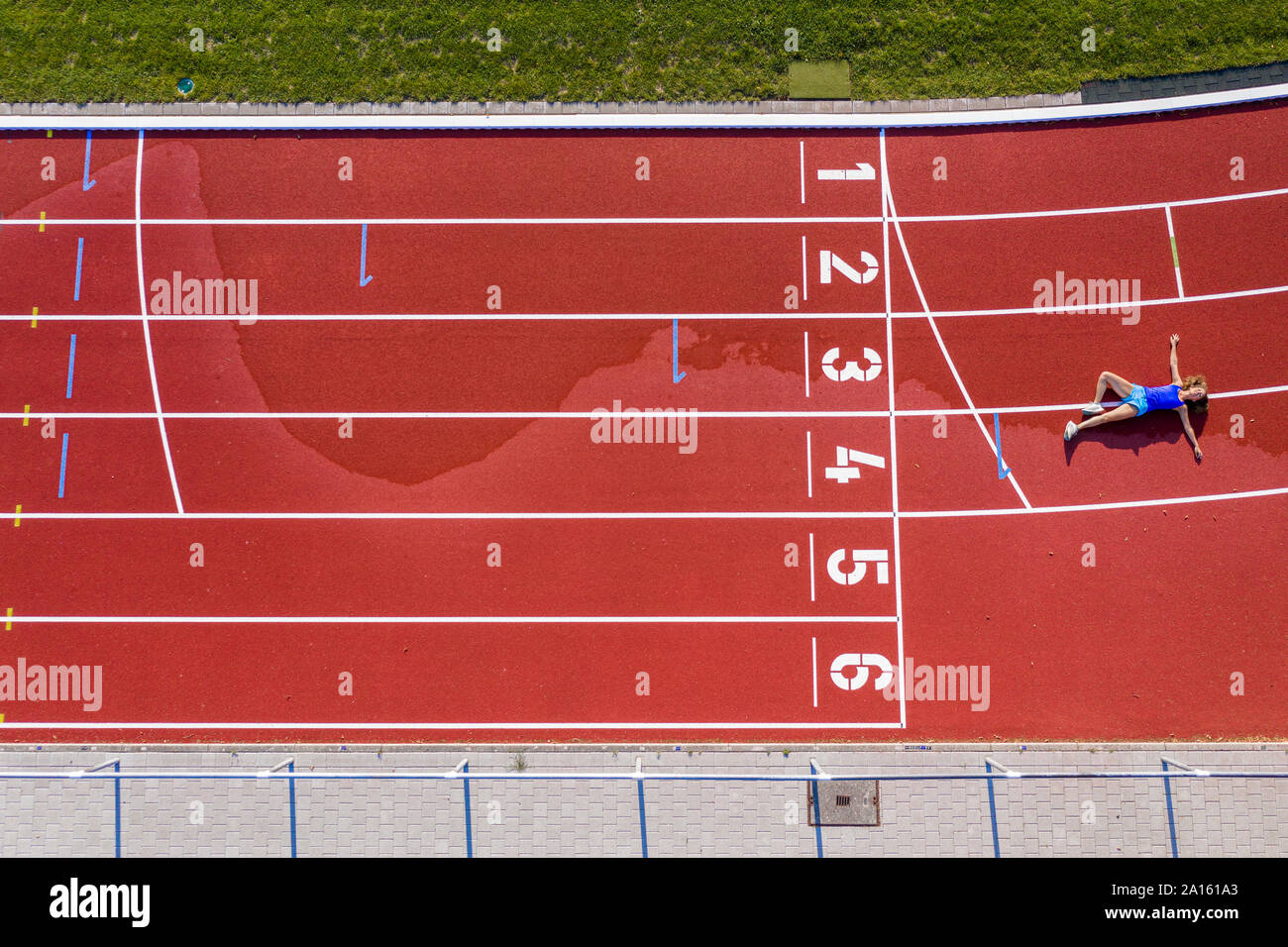 Aerial view of a young female athlete lying on a tartan track after crossing the finishing line Stock Photo