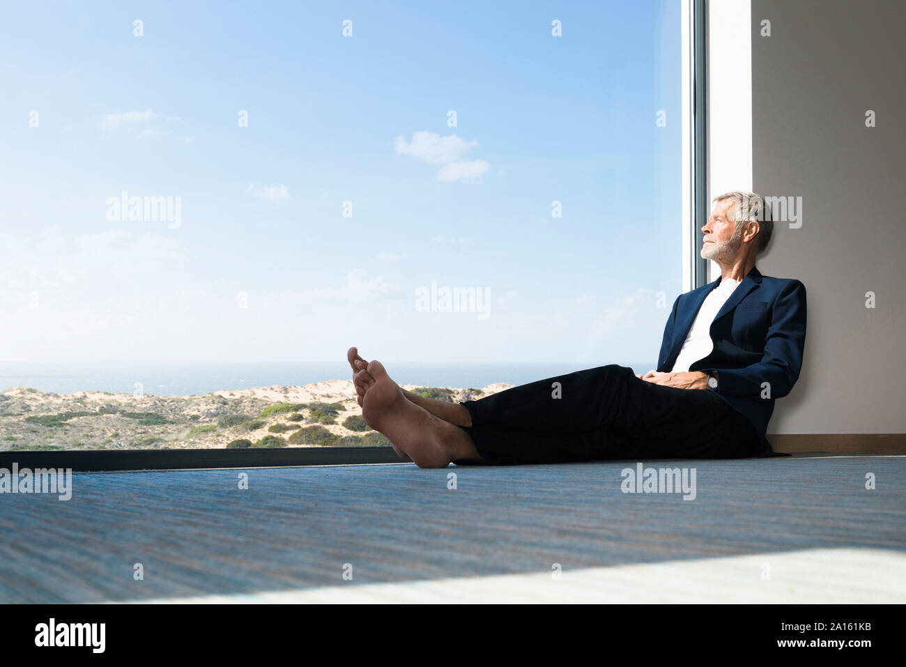 Senior businessman sitting at panorama window looking out Stock Photo