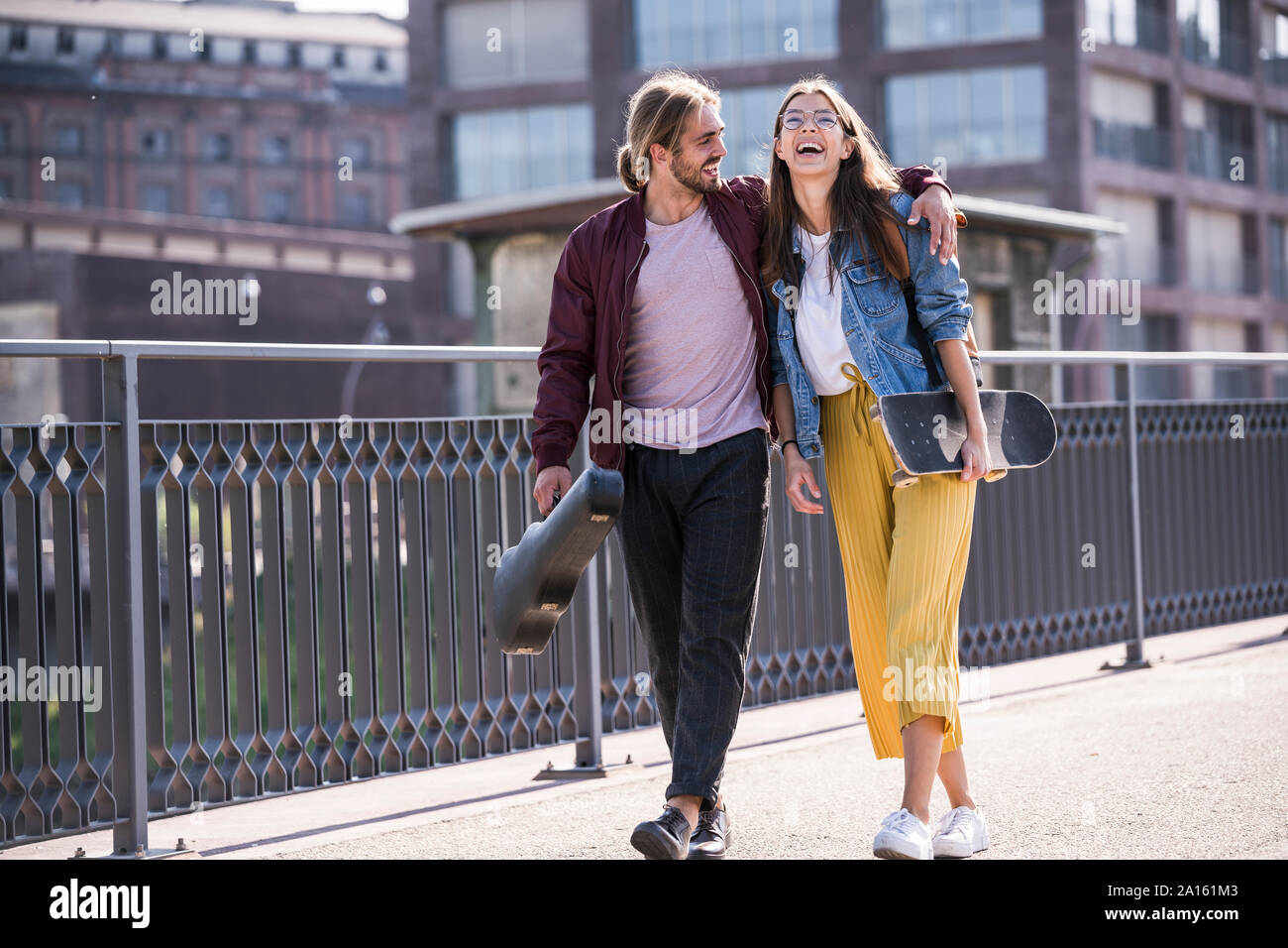 Happy young couple with skateboard walking on a bridge Stock Photo