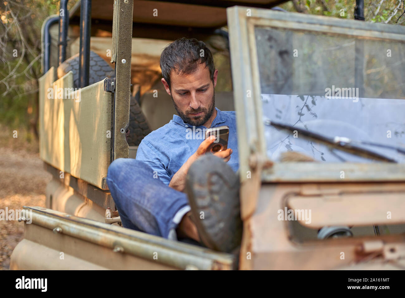 Man sitting in by off-road car, using smartphone Stock Photo