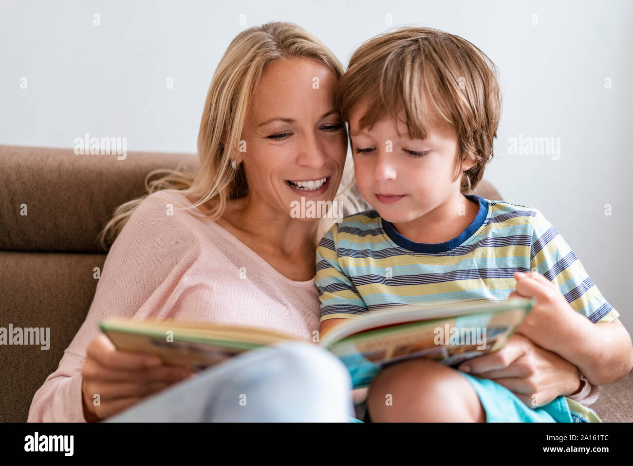 Mother and son reading a book together on couch at home Stock Photo