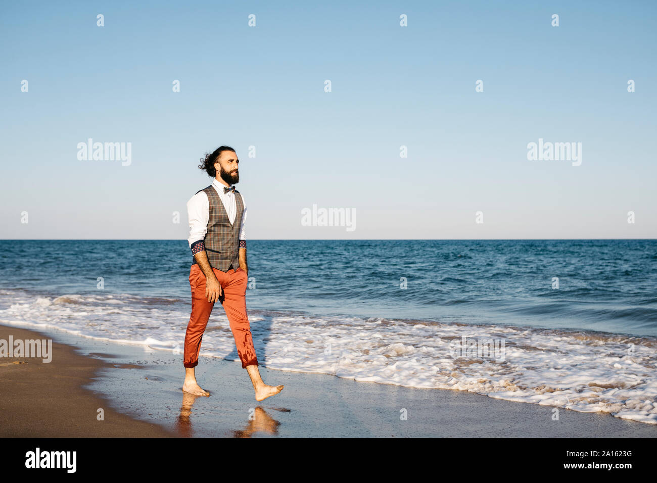 Well dressed man walking on a beach at water's edge Stock Photo
