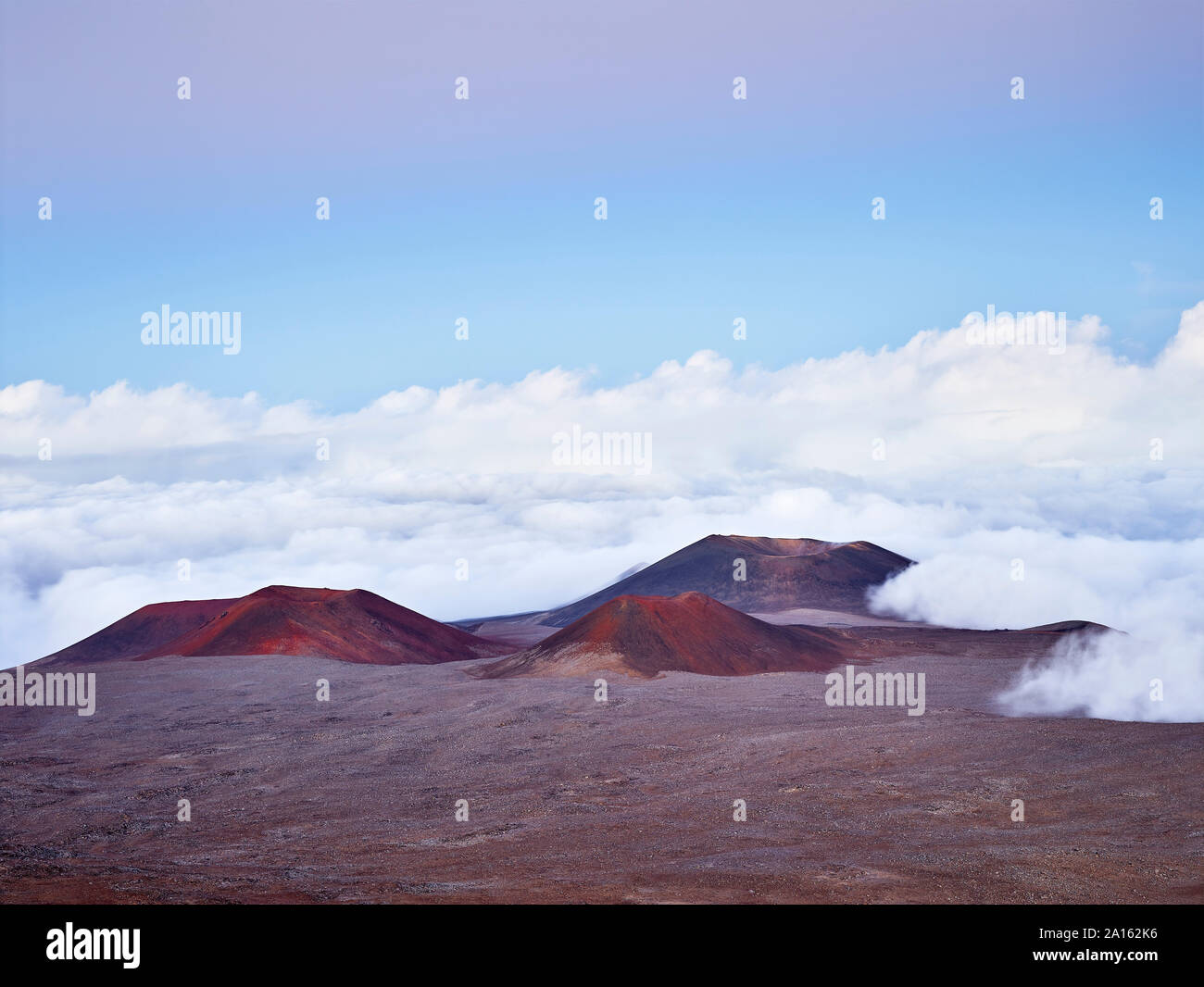 Idyllic view of Mauna Kea volcanic crater amidst clouds against blue sky Stock Photo