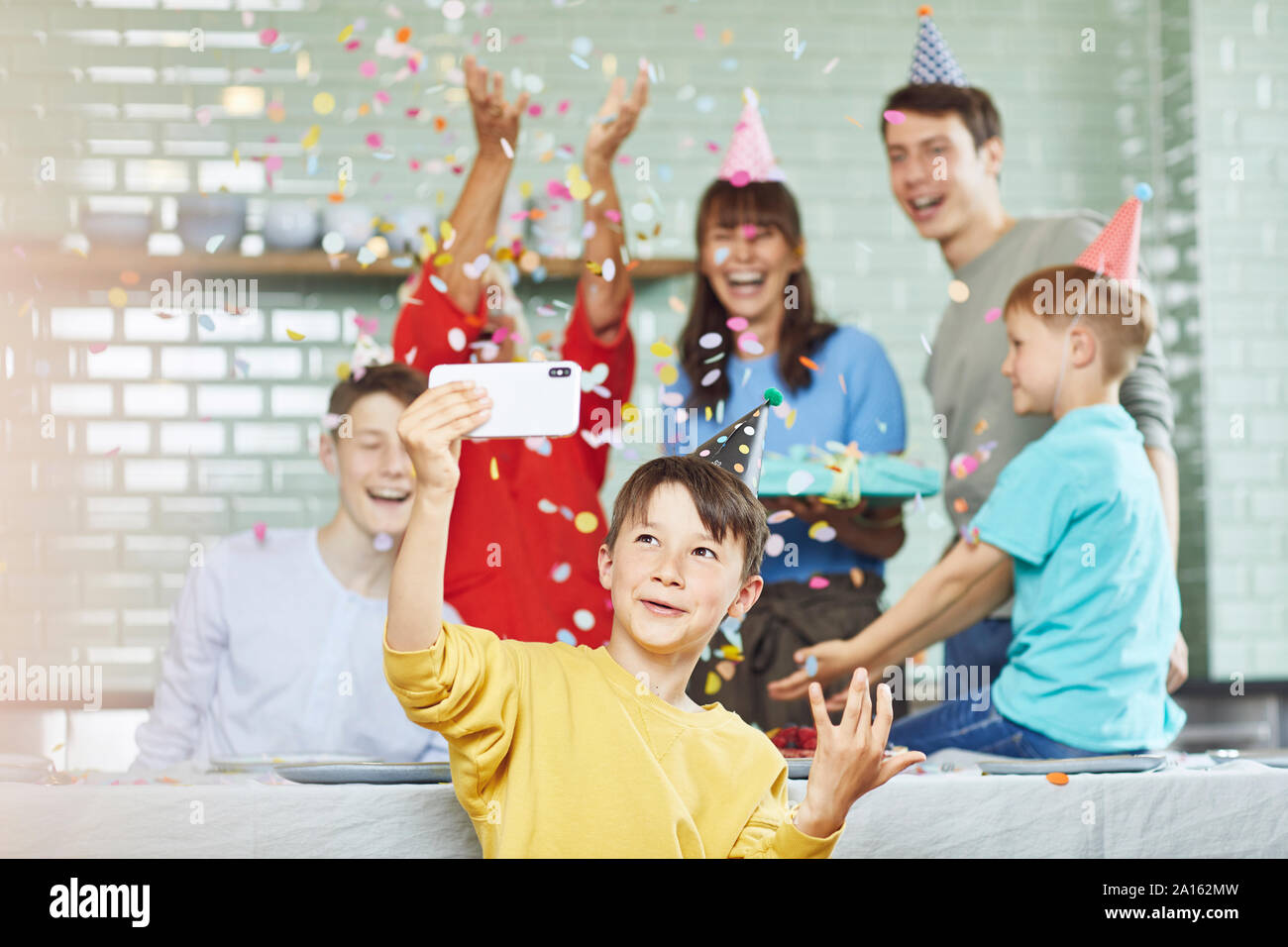 Mother and sons celebrating grandmother's bithday in their kitchen, boy taking selfies Stock Photo