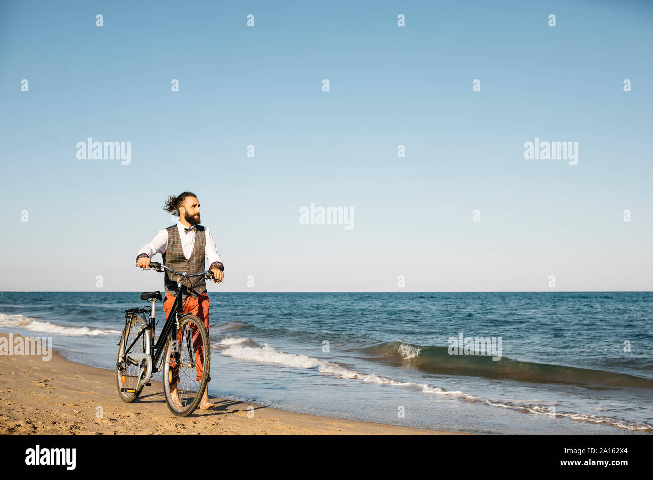 Well dressed man walking with his bike on a beach Stock Photo