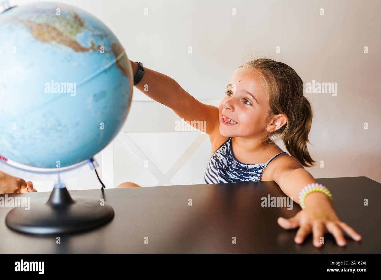 Happy schoolgirl looking at globe on desk Stock Photo - Alamy