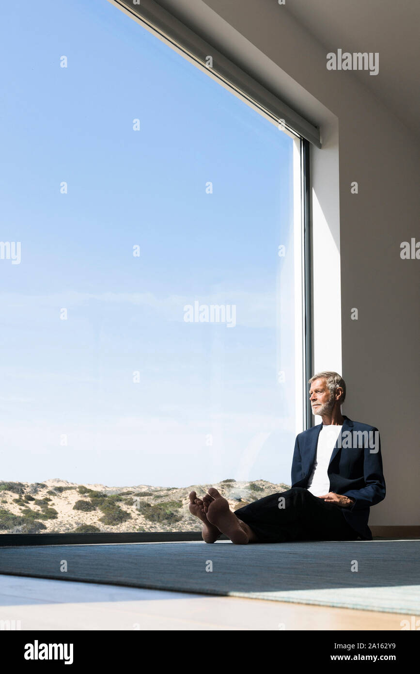 Senior businessman sitting at panorama window looking out Stock Photo