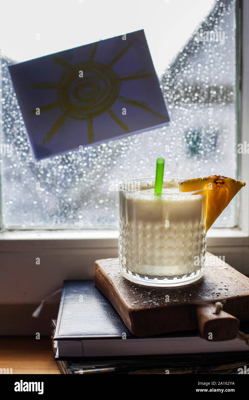 Glass of Pina Colada standing in front of window covered in raindrops Stock Photo