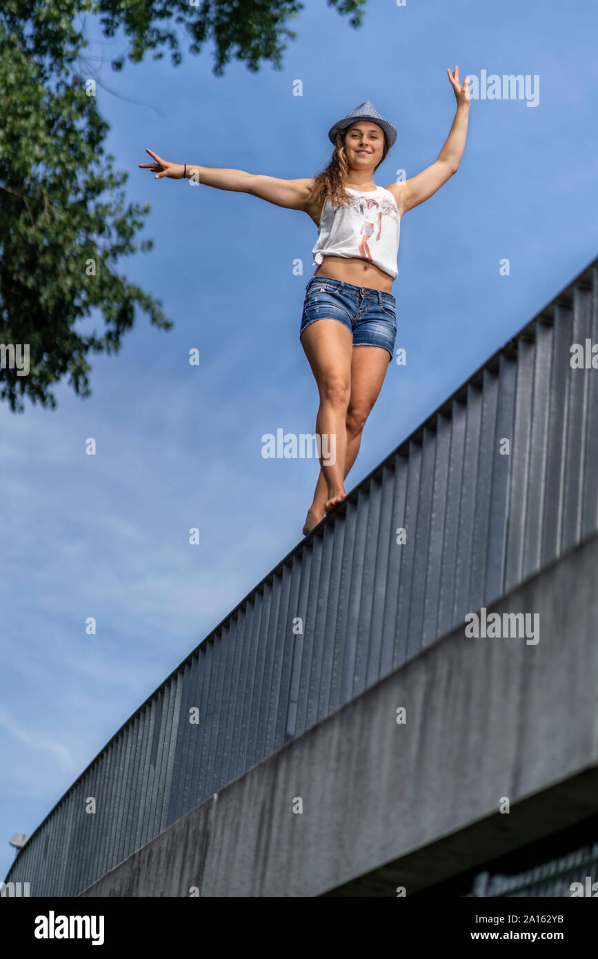 Smiling young woman balancing on a bridge railing Stock Photo
