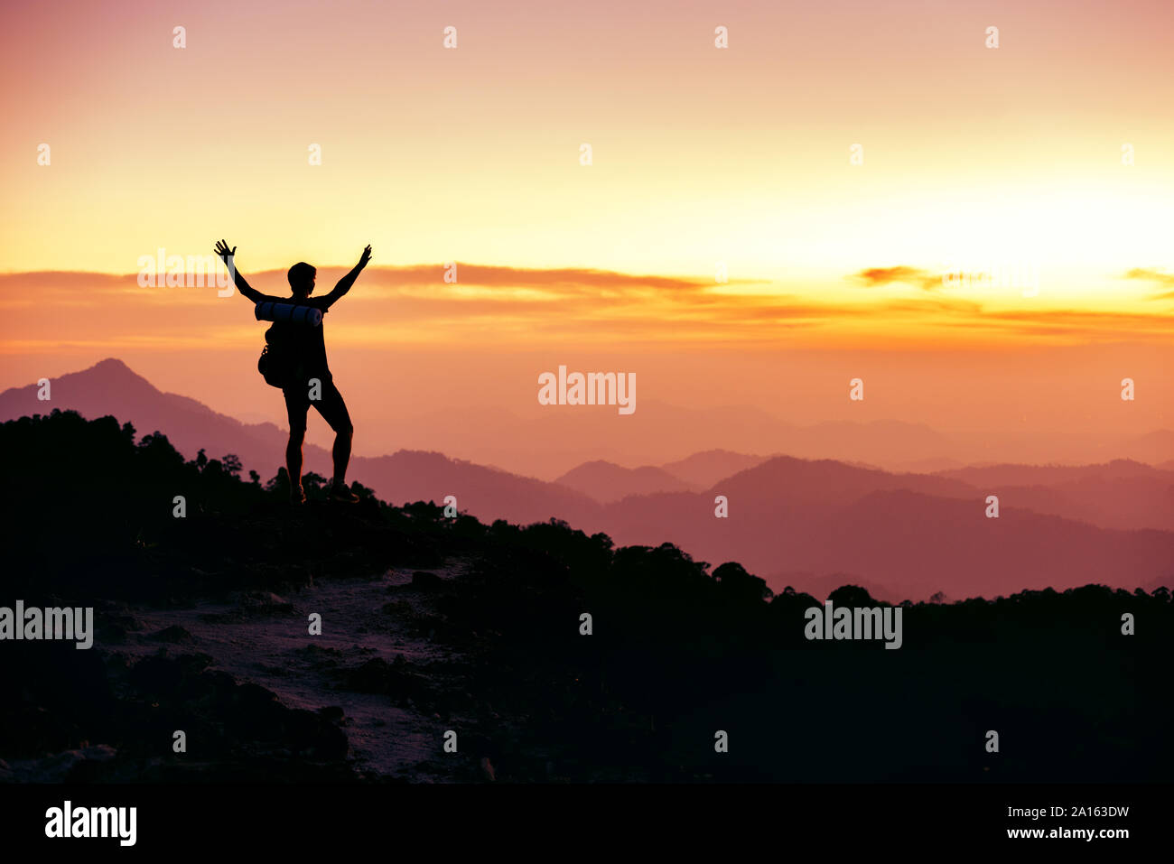 Hikers or travelers silhouette stands on mountain top against sunset with raised arms Stock Photo