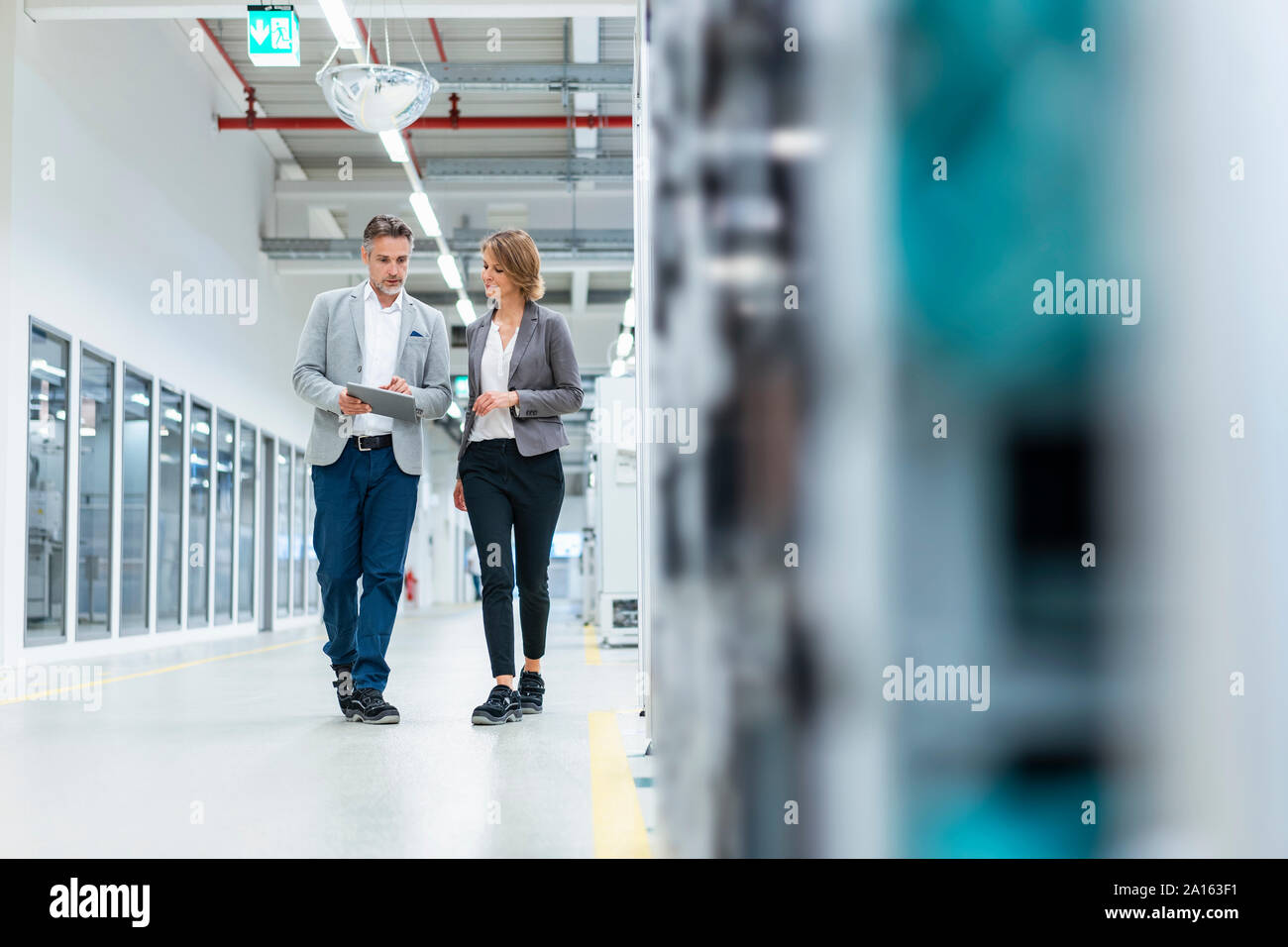 Businesswoman and businessman with tablet walking and talking in a modern factory Stock Photo