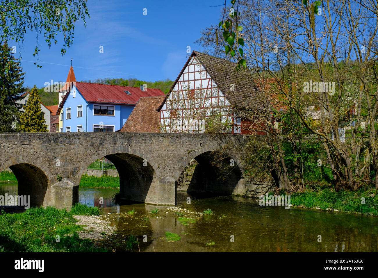 Old arch bridge over Tauber river with town houses in background, Adelshofen, Bavaria, Germany Stock Photo