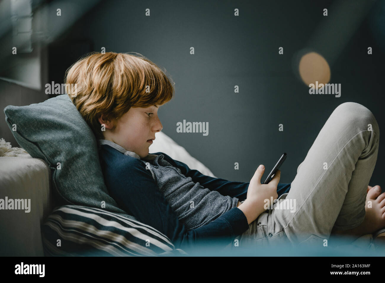 Redheaded boy lying on couch looking at cell phone Stock Photo