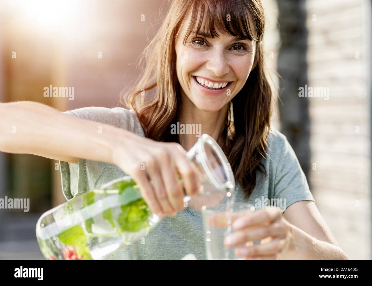 Portrait of happy woman pouring infused water into glass Stock Photo