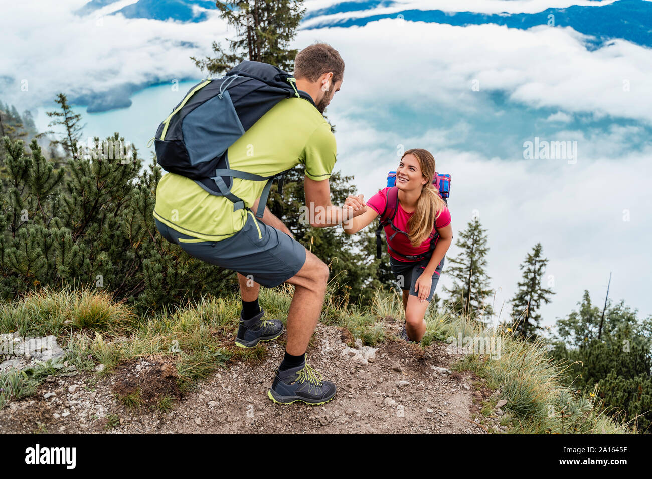 Young man helping girlfriend on a hiking trip in the mountains, Herzogstand, Bavaria, Germany Stock Photo