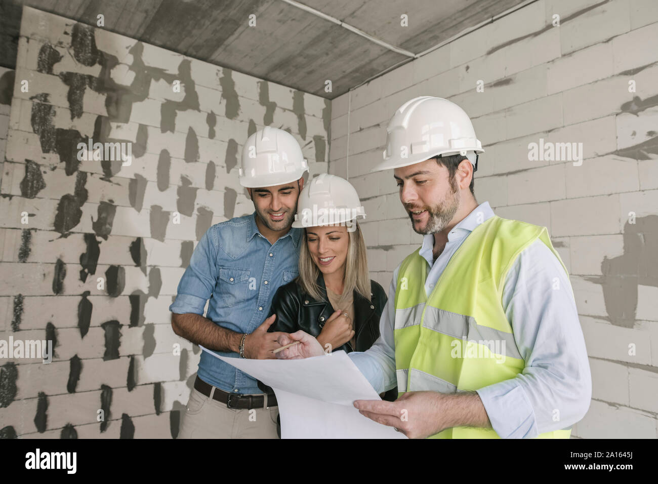 Architect talking about architectural plan with future owners on construction site Stock Photo