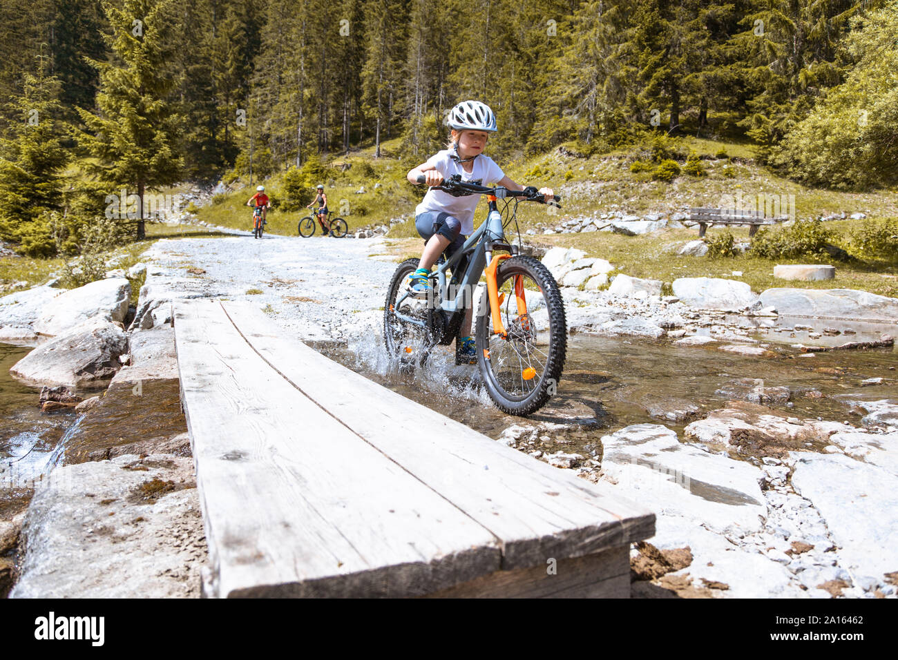Girl crossing a mountain stream with her e-mountain bike Stock Photo