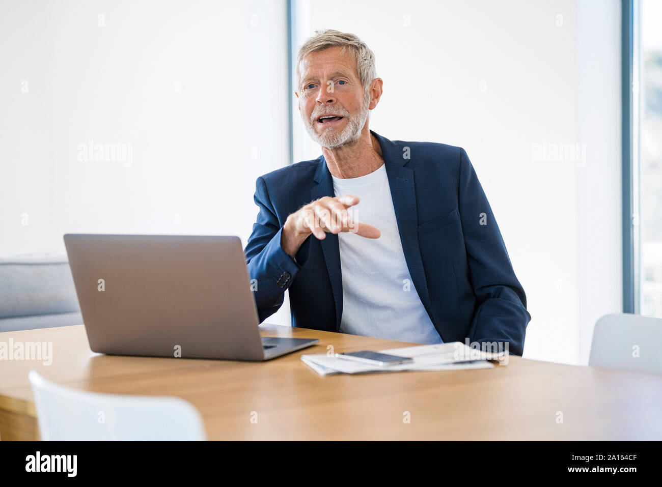 Senior businessman with laptop sitting at desk at home talking Stock Photo