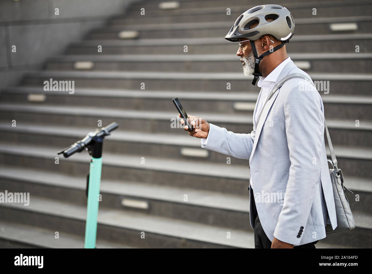 Mature businessman with E-Scooter wearing cycling helmet looking at cell phone Stock Photo