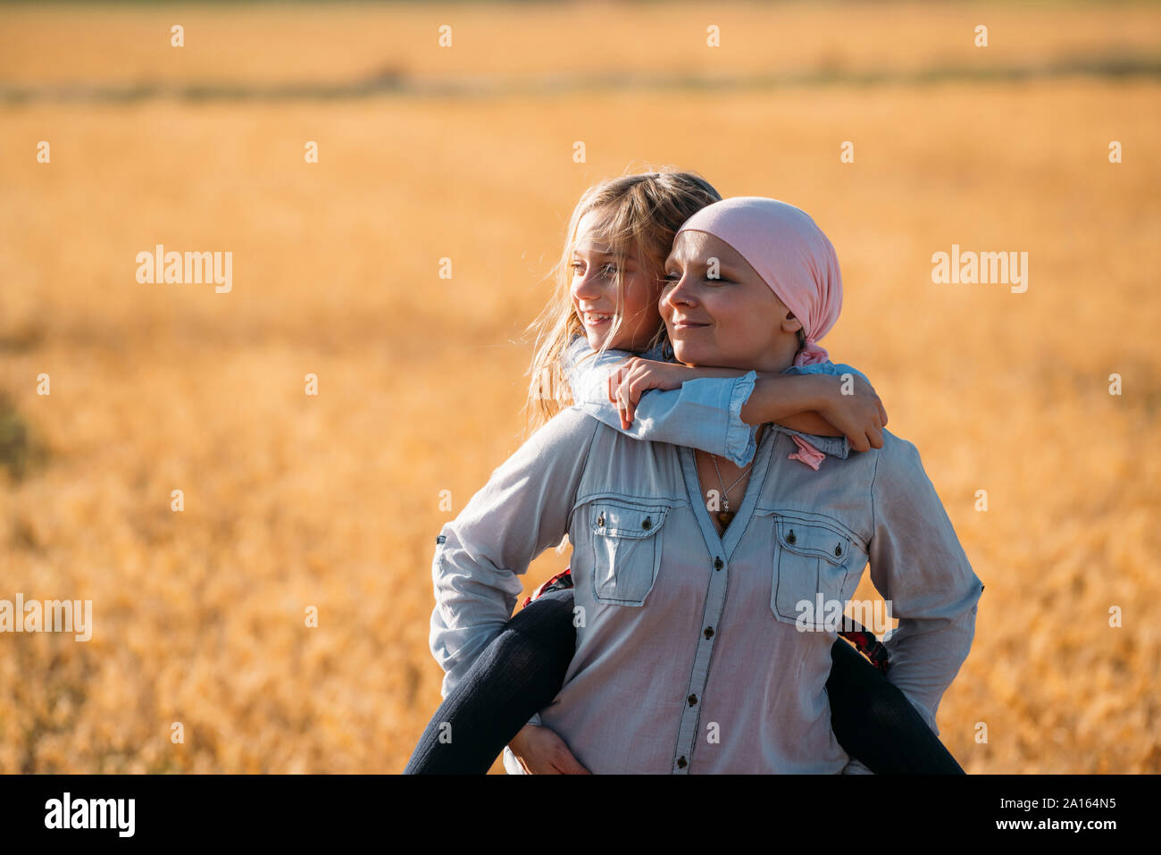 A woman with cancer carrying her daughter on her back, looking sideways Stock Photo