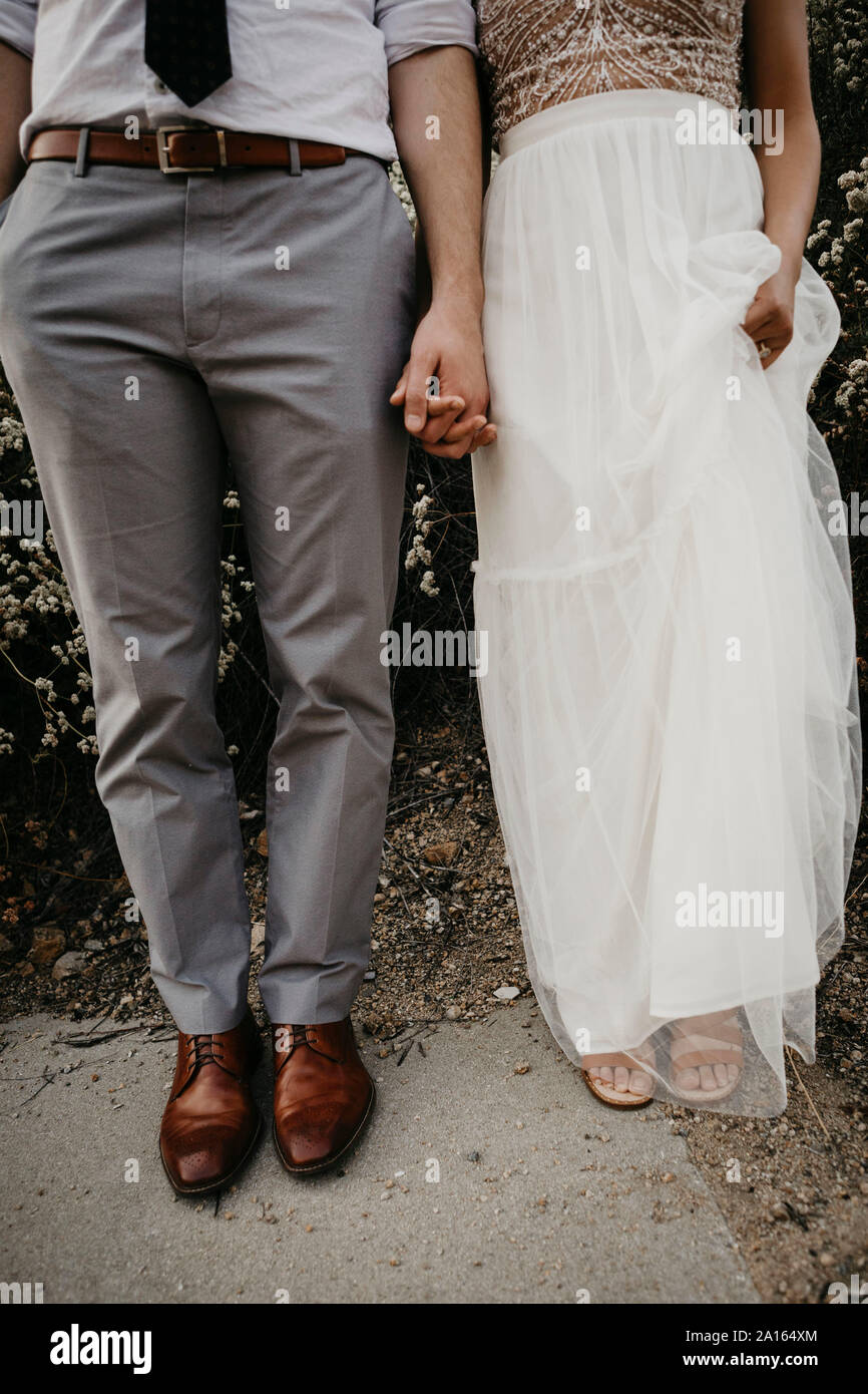 Low section of bride and groom holding hands outdoors Stock Photo